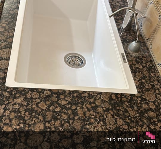 כיור לבן על משטח שיש כהה עם ברז כסוף